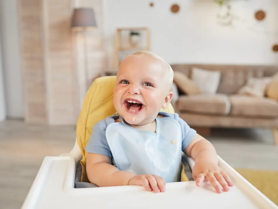 Smiling baby in high chair, supporting baby feeding tips and nutrition advice for first foods